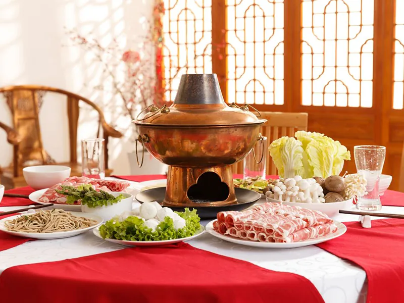 Authentic copper hot pot surrounded by fresh ingredients like lamb rolls, noodles, and mushrooms at Beijing Hot Pot Restaurant, a Hot Pot Restaurant in Portland