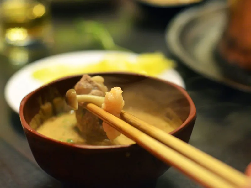Chopsticks holding cooked hot pot ingredients dipped in rich sesame sauce at Beijing Hot Pot Restaurant, a Hot Pot Restaurant in Portland