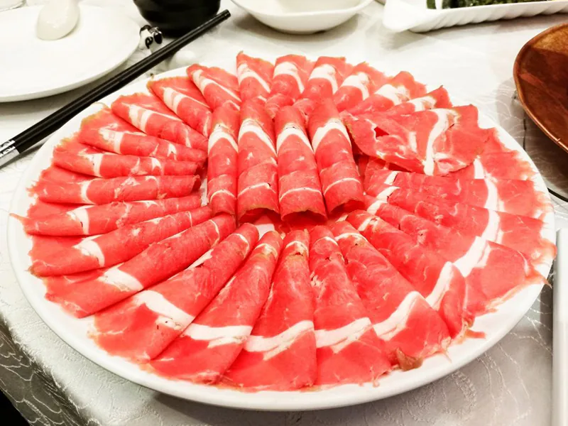 Artfully arranged sliced lamb rolls on a white plate, ready for hot pot cooking at Beijing Hot Pot Restaurant, a Hot Pot Restaurant in Portland
