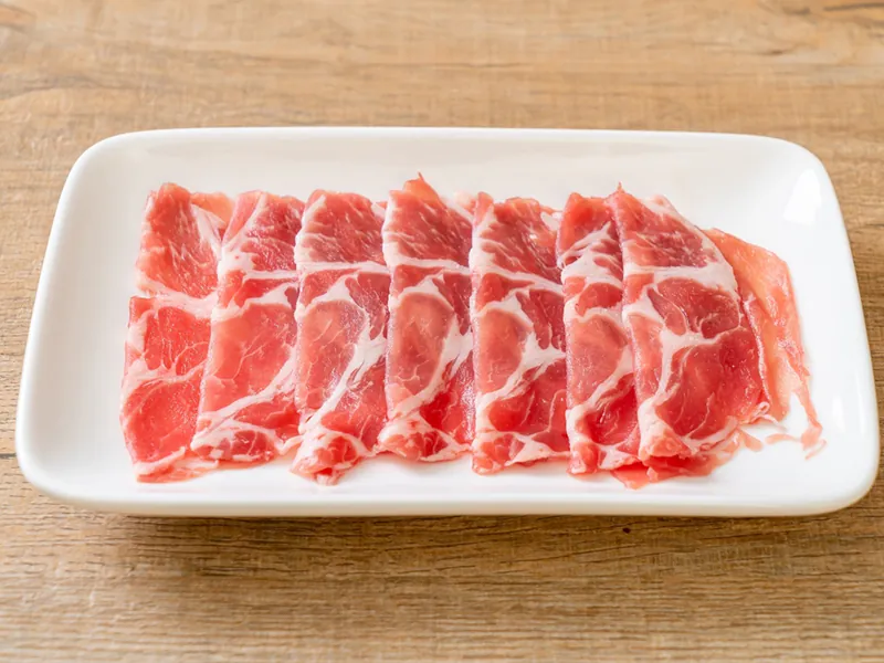 Thinly sliced marbled pork on a white plate, ideal for hot pot at Beijing Hot Pot Restaurant, a Hot Pot Restaurant in Portland